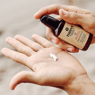 A man holding a bottle of Thrive beard oil, showcasing grooming and self-care for a well-maintained beard.
